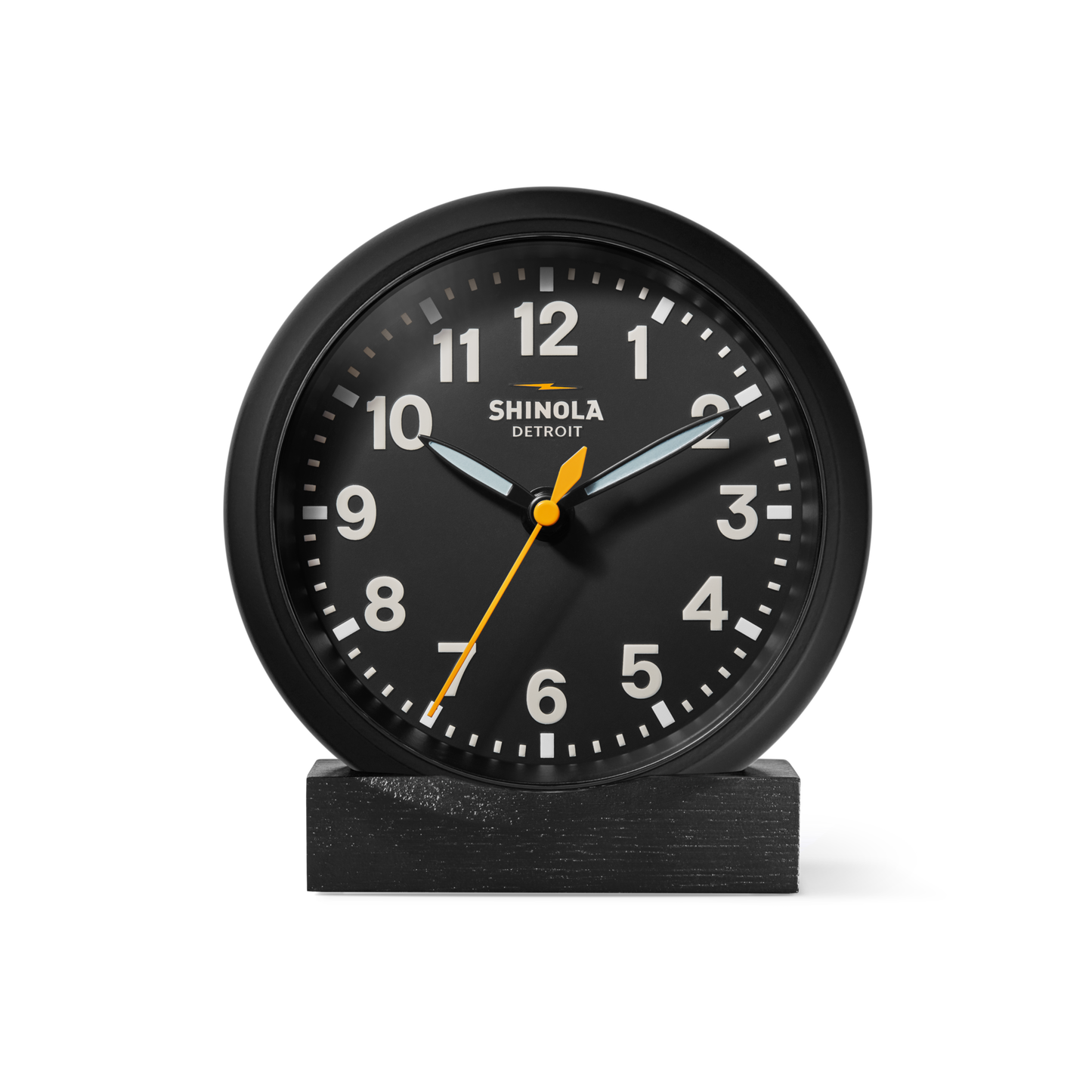 The Shinola 6" Runwell Clock features a black analog face with white numerals, white hour and minute hands, and a yellow second hand. It sits on an oak stand, highlighting Shinola craftsmanship against a white background.