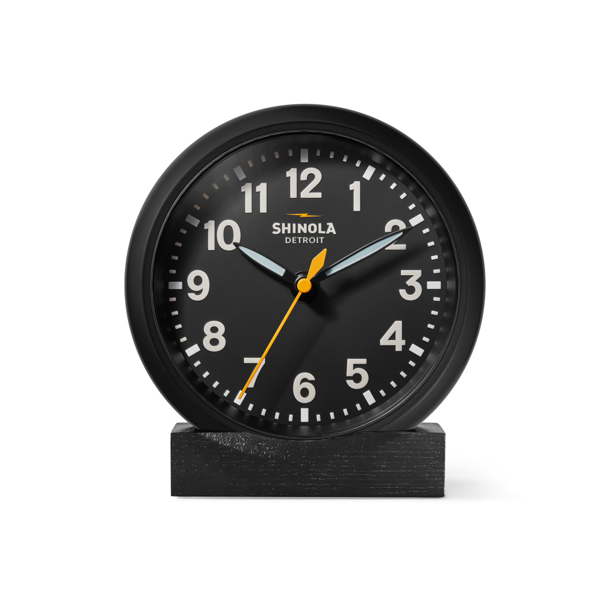 The Shinola 6" Runwell Clock features a black analog face with white numerals, white hour and minute hands, and a yellow second hand. It sits on an oak stand, highlighting Shinola craftsmanship against a white background.
