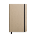 The Shinola Medium Soft Ruled Journal - Oat is shown closed with a textured beige cover, black elastic band on the right, and a black ribbon bookmark against a white background. Features durable smyth-sewn binding.