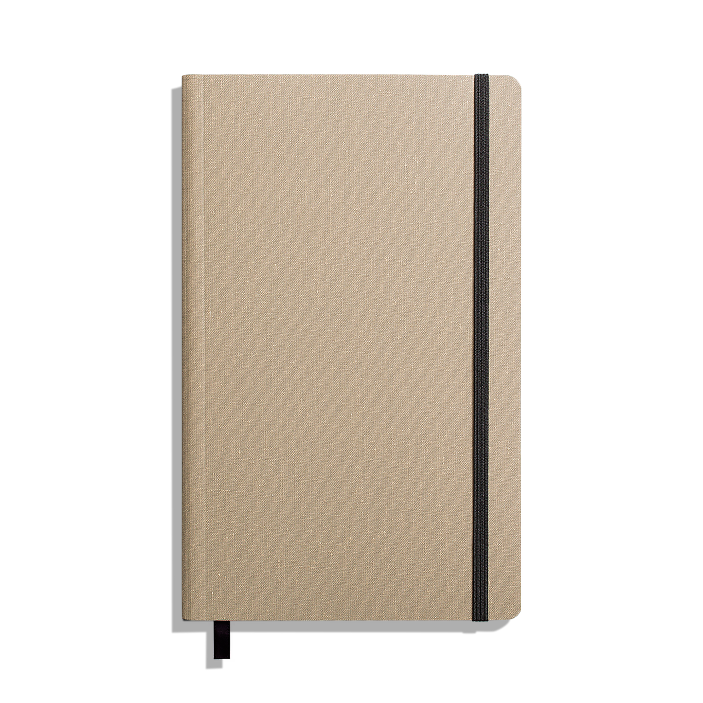 The Shinola Medium Soft Ruled Journal - Oat is shown closed with a textured beige cover, black elastic band on the right, and a black ribbon bookmark against a white background. Features durable smyth-sewn binding.