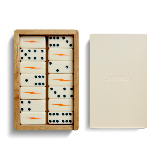 The Shinola Dominoes Set—Cream / Blue includes hand-painted cream tiles with blue dots and orange lightning bolts, presented in a wooden box beside a cream lid embossed with the Shinola logo.