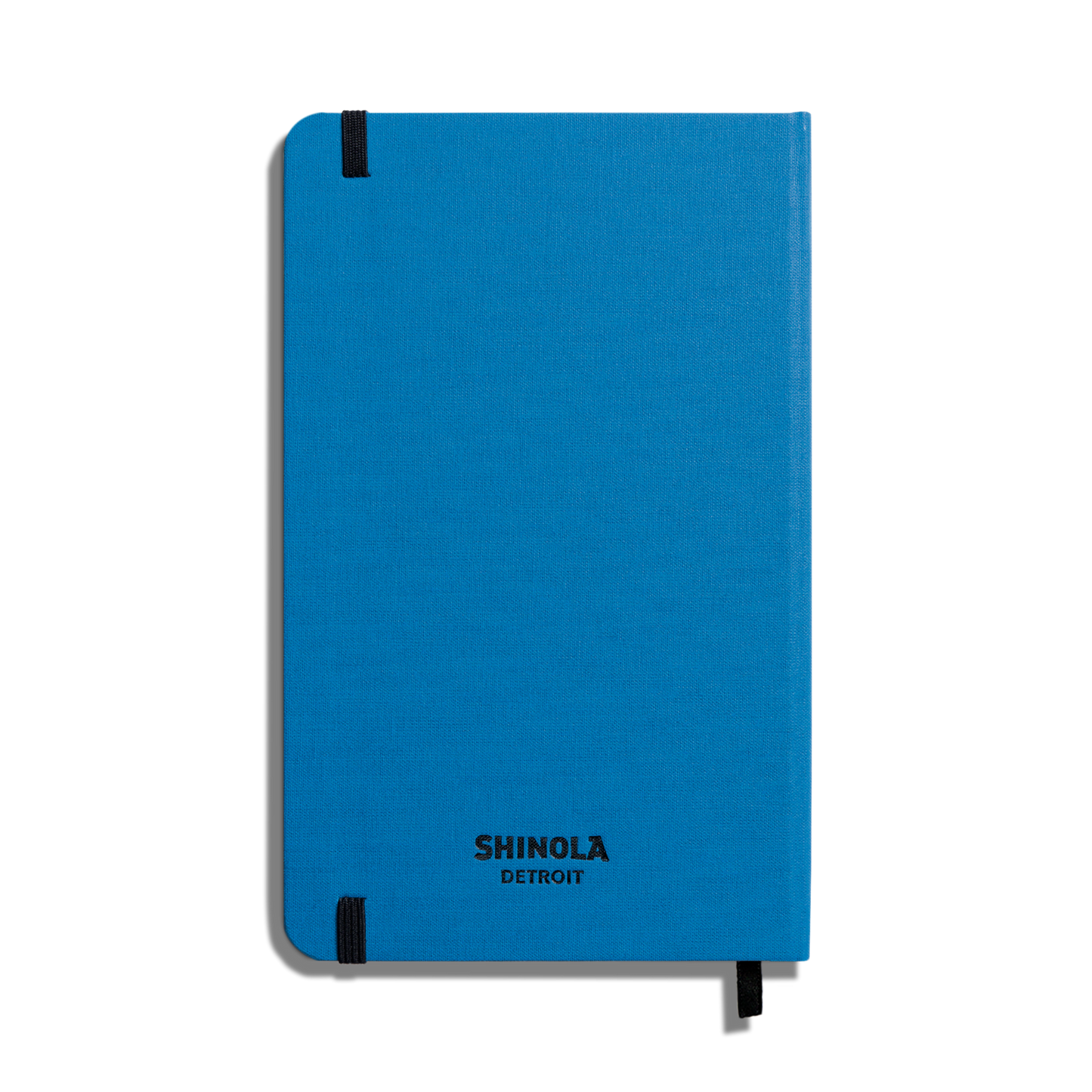 A closed Shinola Medium Hard Ruled Journal in cobalt with smyth-sewn binding and black elastic bands on two corners, shown against a white background.