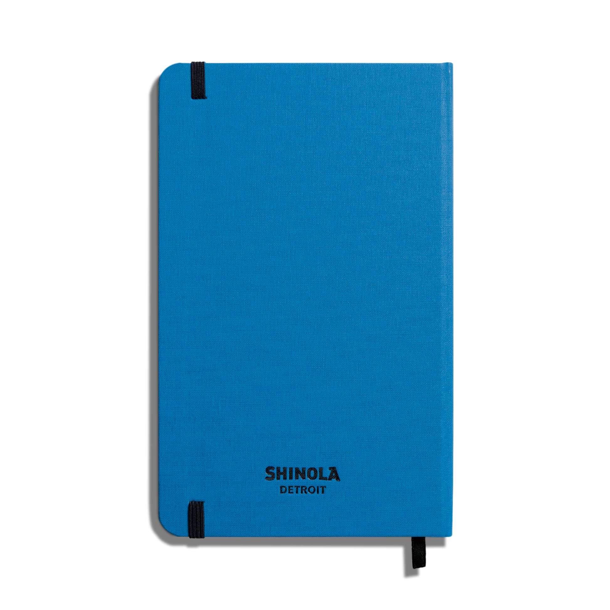 A closed Shinola Medium Hard Ruled Journal in cobalt with smyth-sewn binding and black elastic bands on two corners, shown against a white background.
