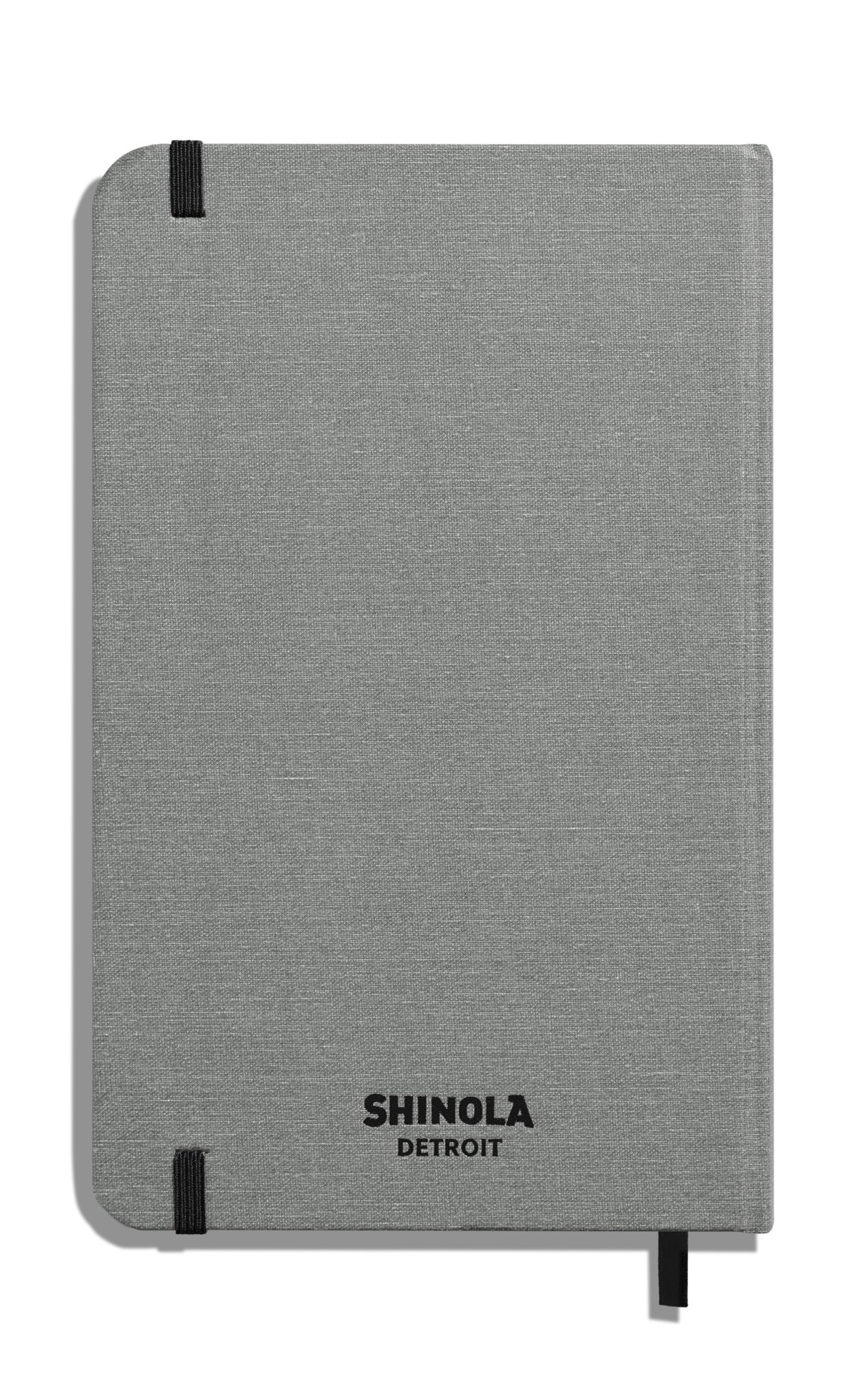 The Shinola Medium Hard Ruled Journal - Stone features a gray linen cover, smyth-sewn binding, black elastic bands on the top and bottom left corners, and "Shinola Detroit" printed in black at the bottom center.