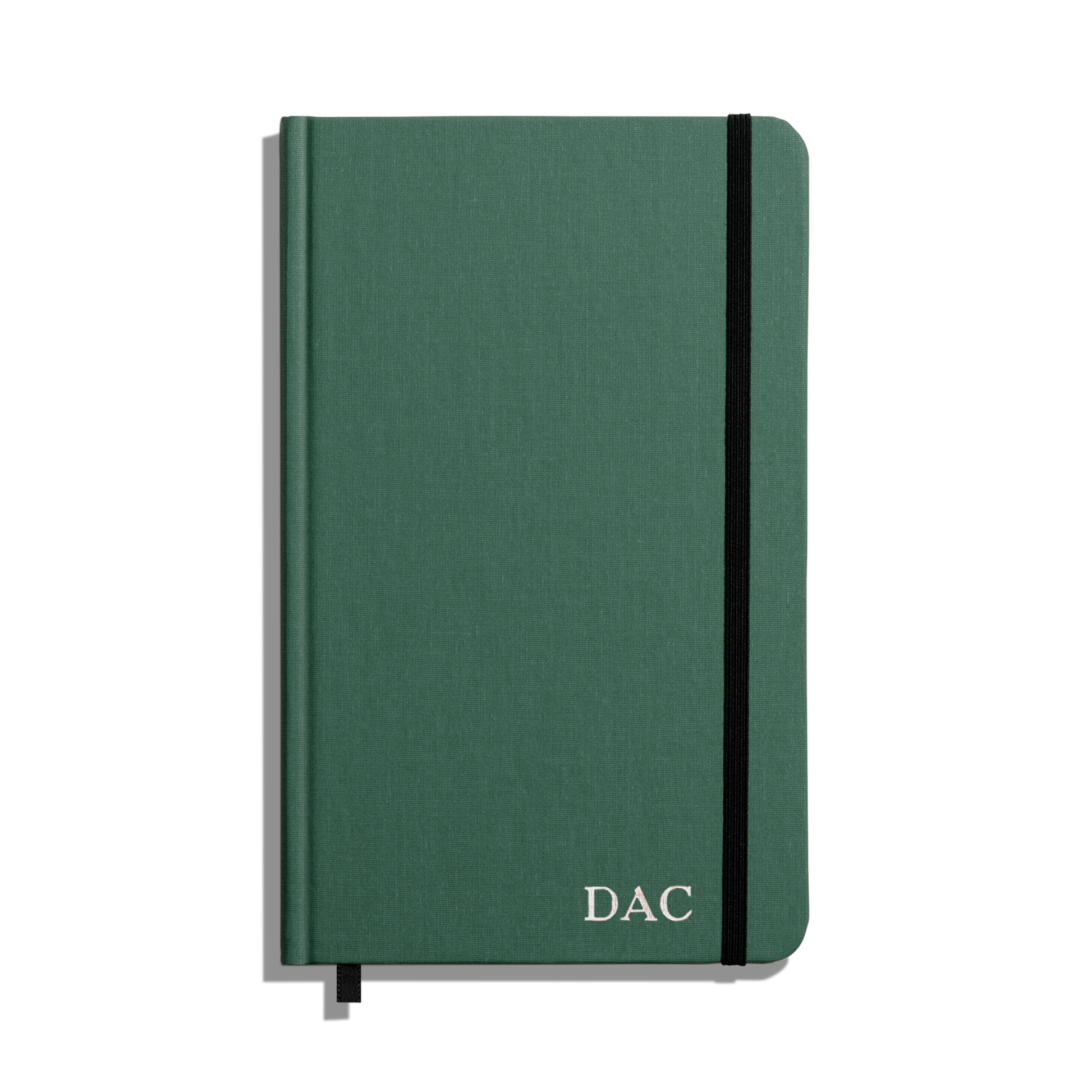 The Shinola Medium Hard Ruled Journal - Fern is a green linen hardcover notebook with a black elastic band, acid-free paper, ribbon bookmark, and white DAC initials embossed on the front cover’s bottom right corner.