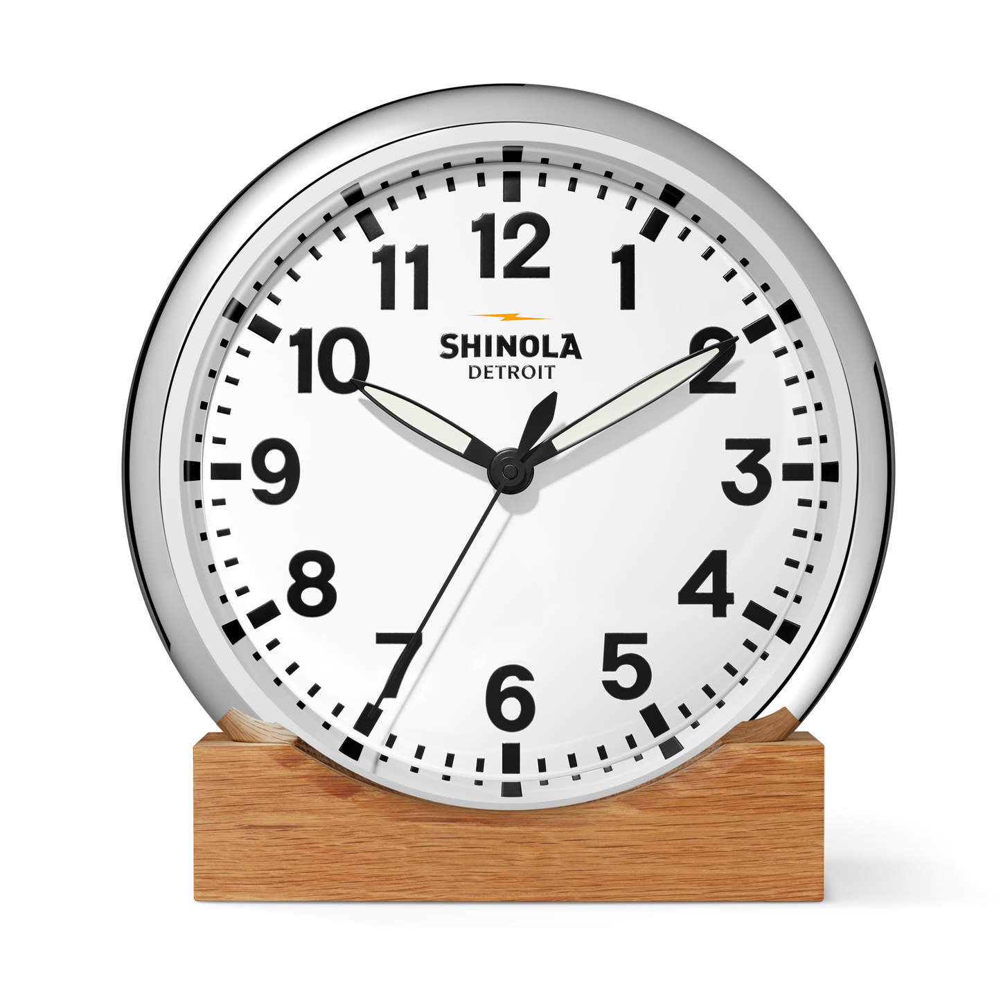 A 14" Shinola Runwell Clock with a white face, black numbers, and a silver frame sits on a wooden base. The clock shows 1:51:34, with the Shinola brand printed on the face.
