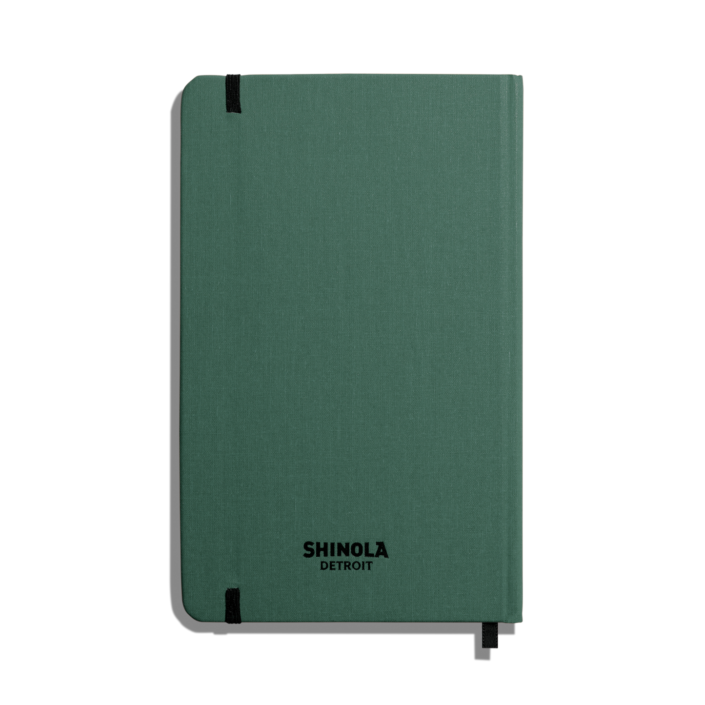 The Shinola Medium Hard Ruled Journal - Fern is a green hardcover notebook with rounded corners, smyth-sewn binding, a top-left elastic band, SHINOLA DETROIT in black on the cover, and a ribbon bookmark at the bottom.