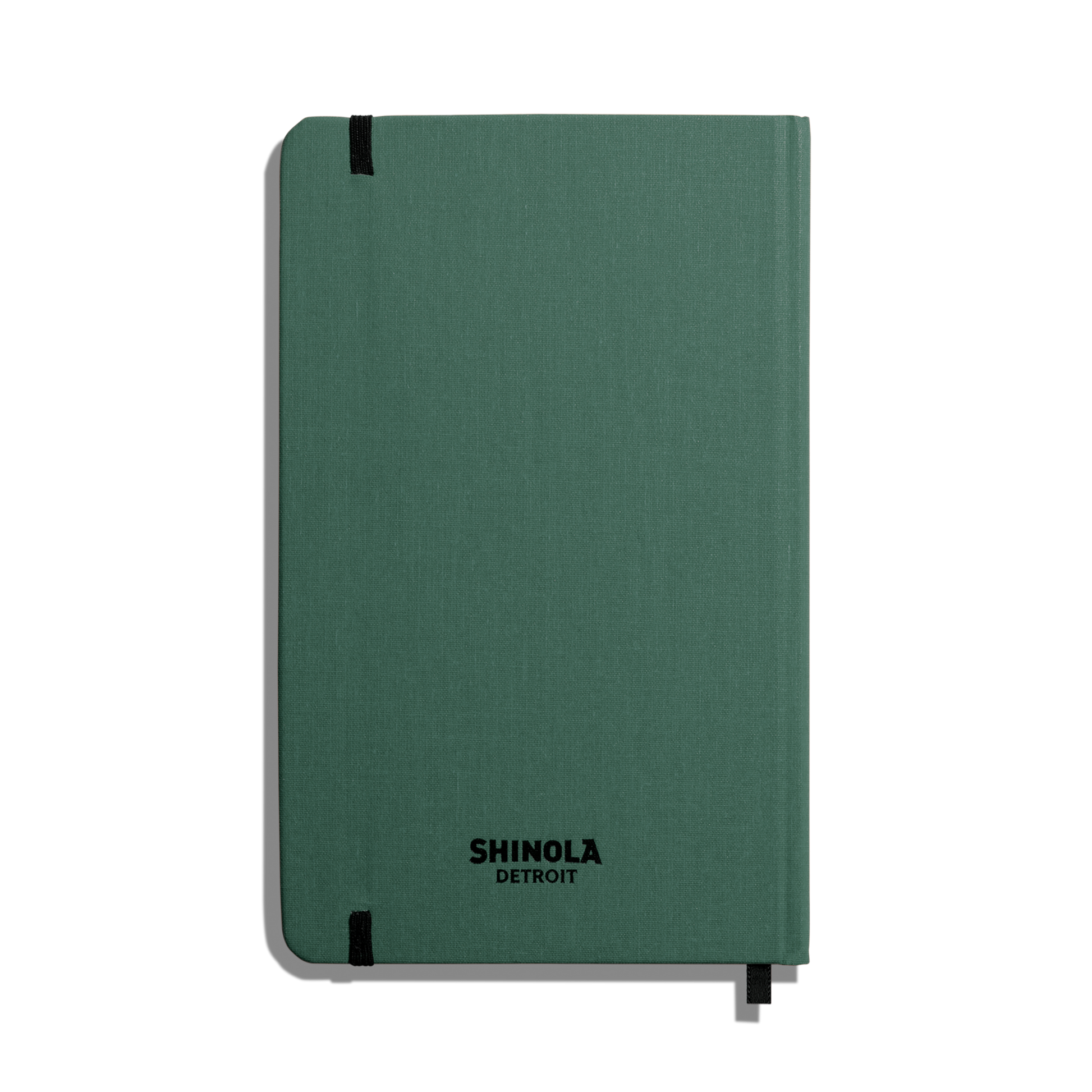 The Shinola Medium Hard Ruled Journal - Fern is a green hardcover notebook with rounded corners, smyth-sewn binding, a top-left elastic band, SHINOLA DETROIT in black on the cover, and a ribbon bookmark at the bottom.