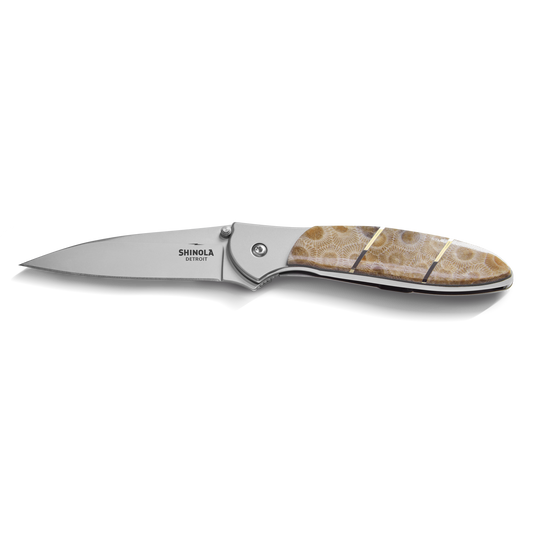 The Shinola + Kershaw Petoskey Stone Pocket Knife features a sharp silver blade and a beige-brown patterned Petoskey Stone handle, with Shinola branding near the hinge, shown on a white background.