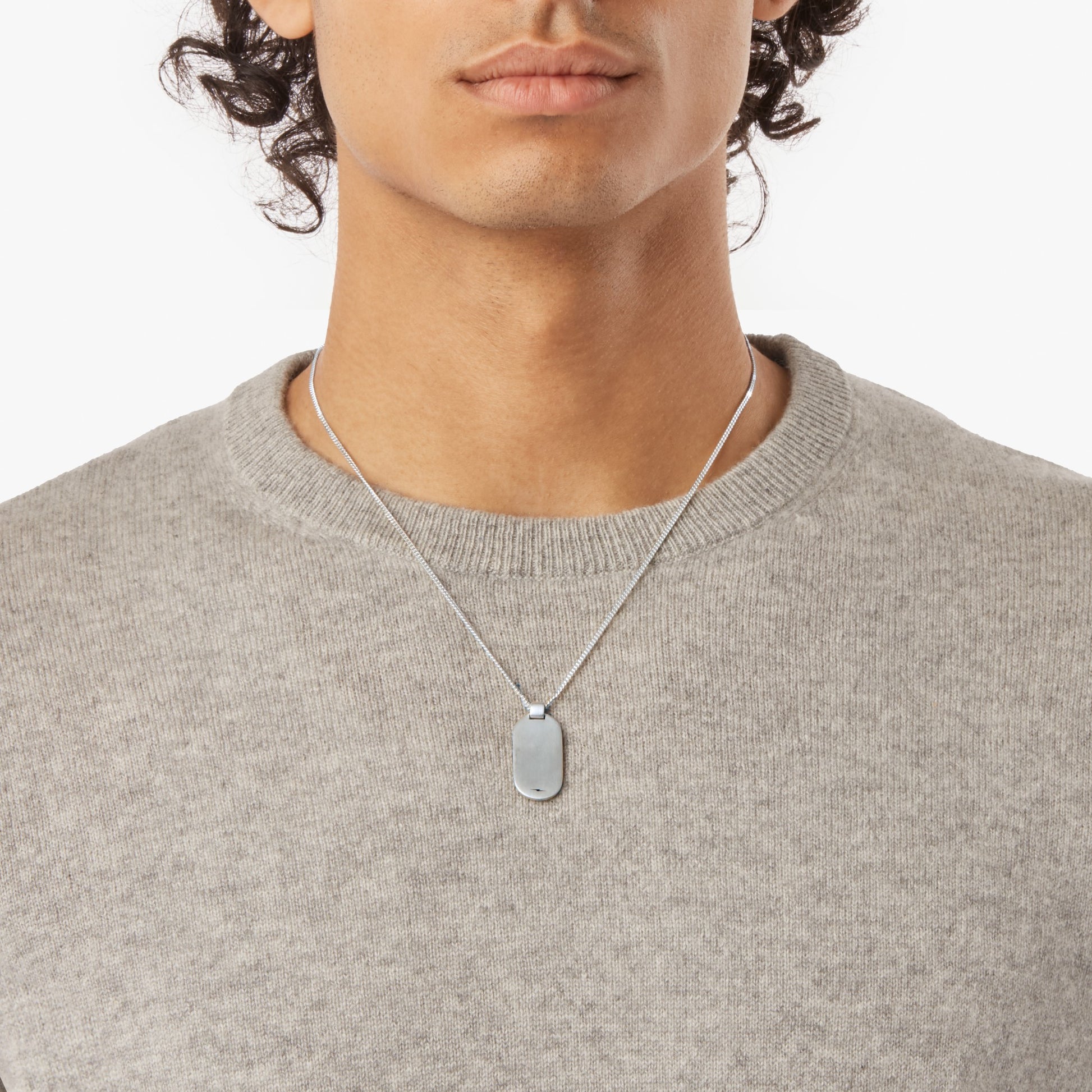 A person is shown from shoulders to just above the lips, wearing a light gray sweater and a Shinola Tag Curb Chain Necklace in sterling silver, against a plain white background.