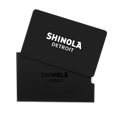 A Physical Gift Card with SHINOLA DETROIT in white lettering is partially inserted into a matching black sleeve embossed with the brand name, both displayed on a white background.