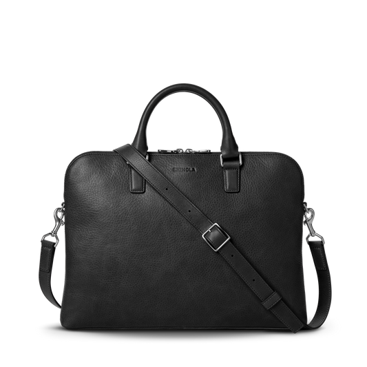 The Shinola Portfolio Briefcase - Black features a slim black leather design with two handles, a detachable shoulder strap, silver hardware, and zip closure, shown against a plain white background.