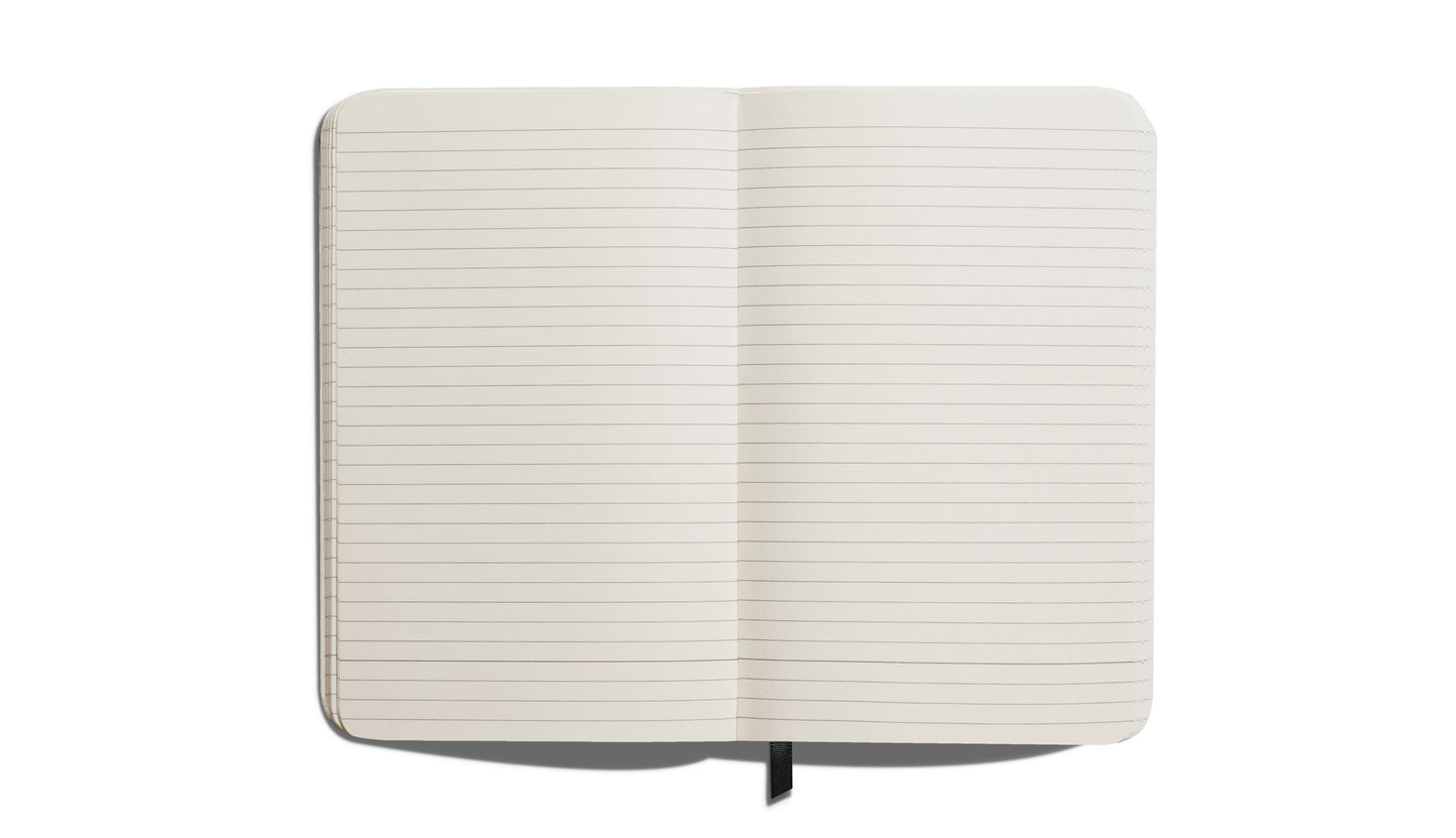 The Shinola Medium Hard Ruled Journal - Stone features acid-free lined pages, smyth-sewn binding, a hard linen cover, and a black ribbon bookmark. It lies flat on a white background, open to reveal its quality craftsmanship.